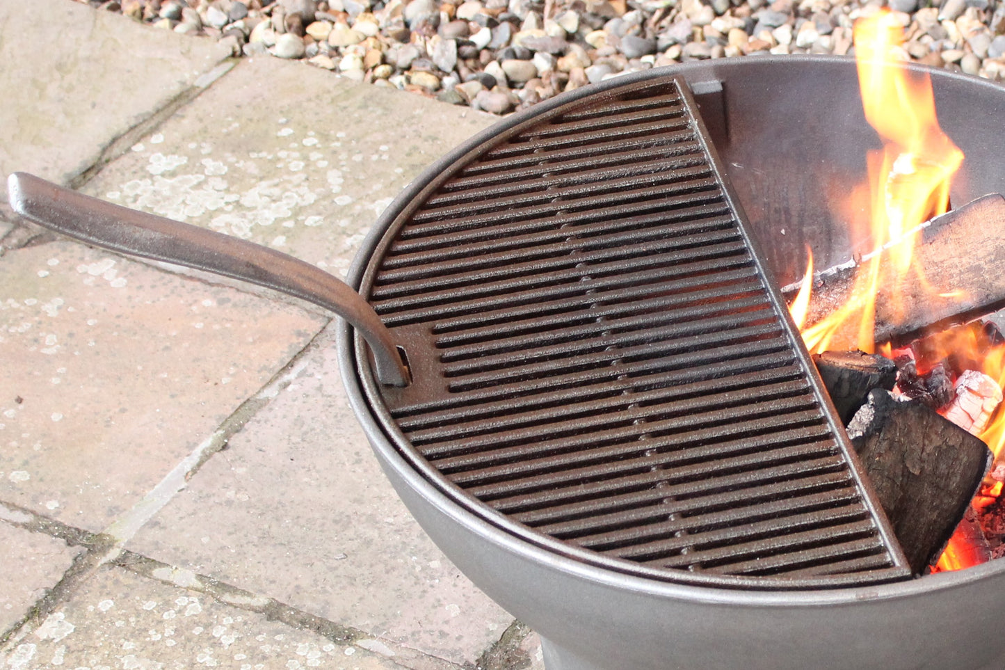 Close-up of a round grill with a cooking grate and a fire burning in the other half.