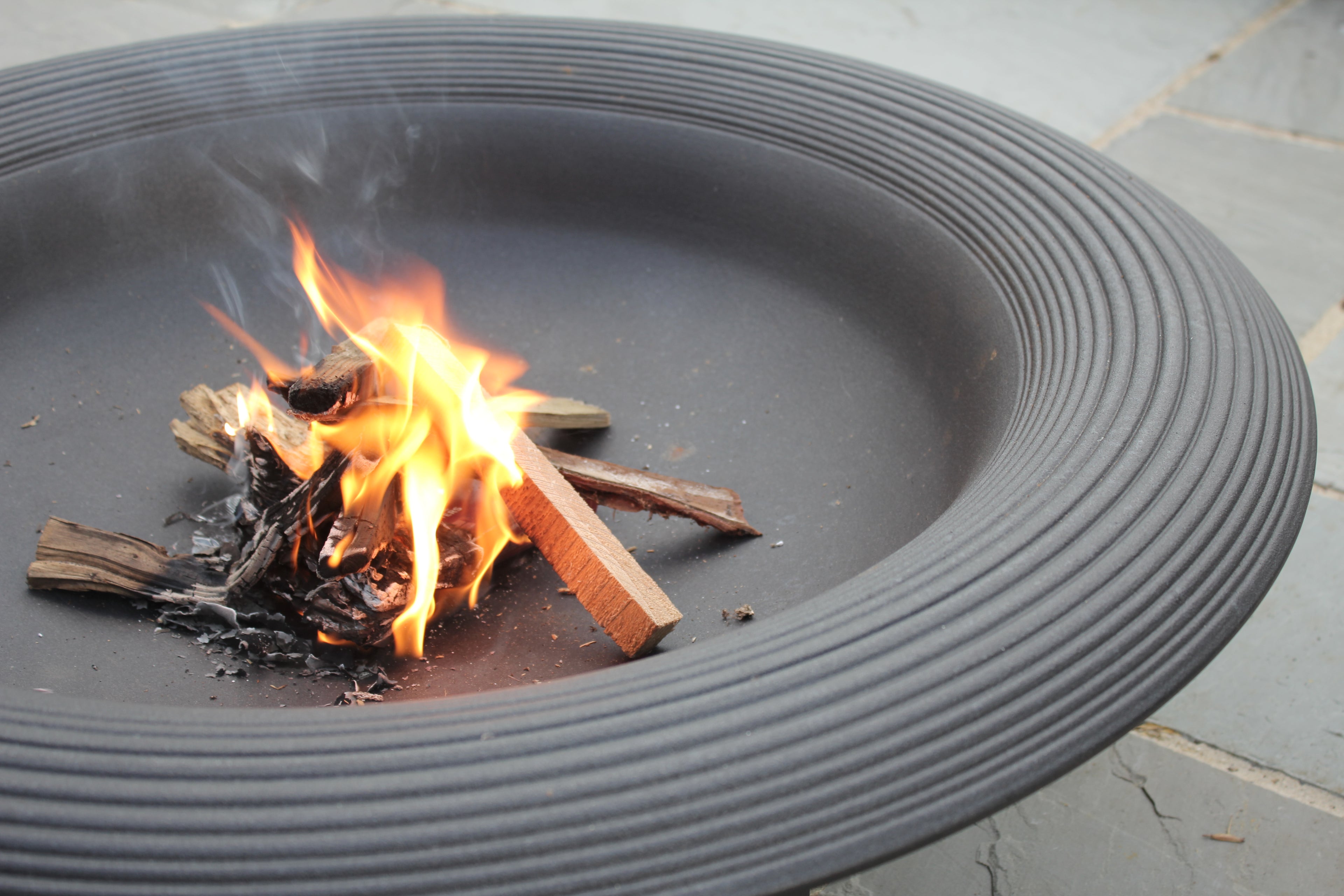 A close-up view of a black fire pit with small flames and logs burning.