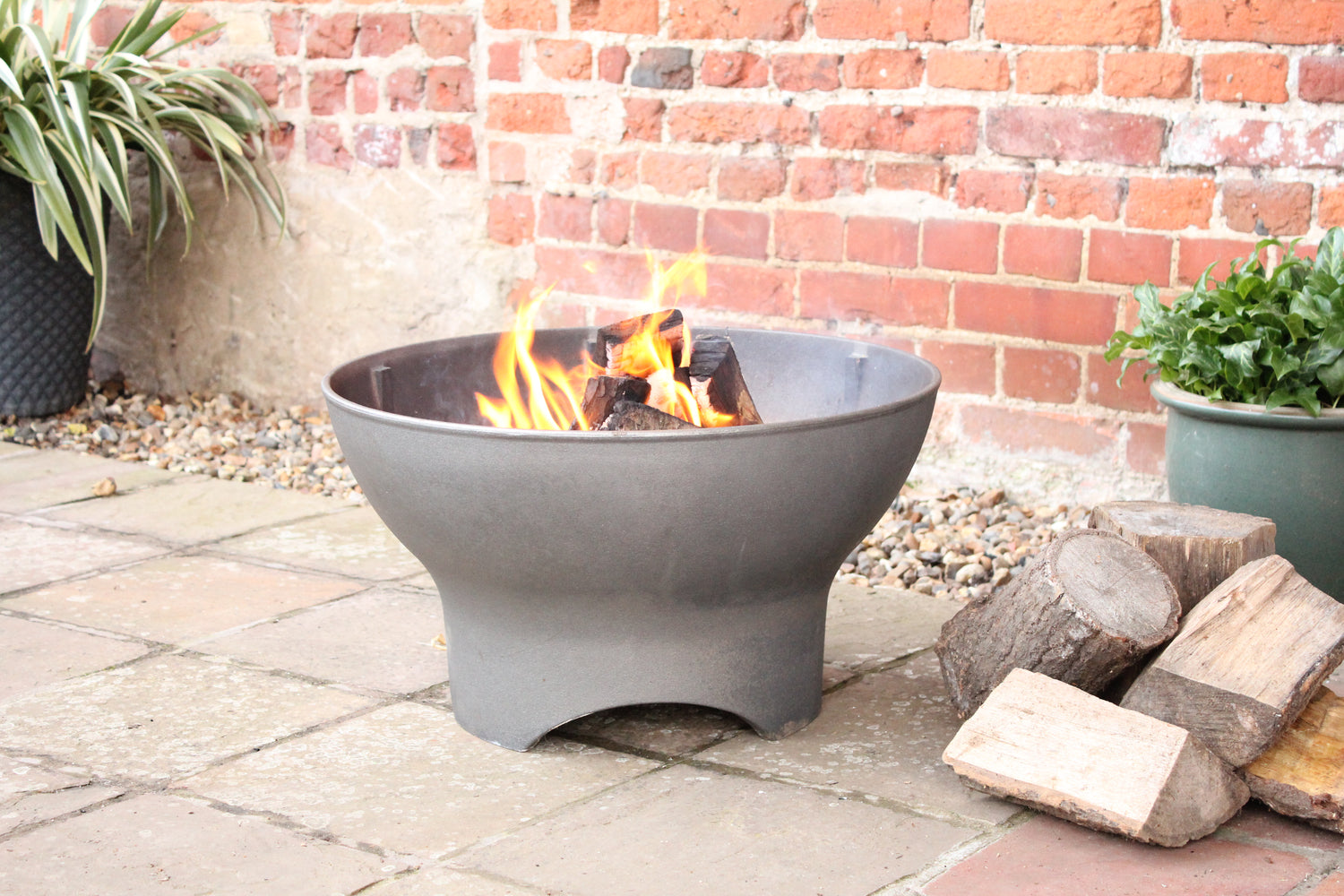 A dark gray fire pit with a roaring fire in a backyard setting.